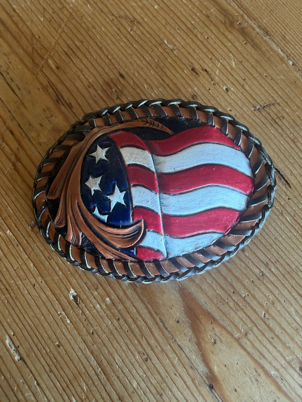 America 250 Trophy Buckle - front with hand-painted American flag, scroll tooling, and braided lace border